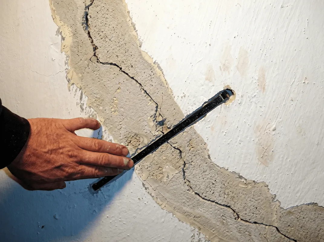 A wall with a large crack is being inspected by a professional in Grand Rapids, MI